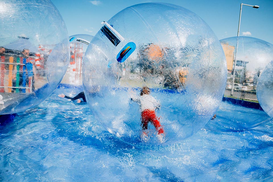 Children have fun, rolling around inside giant plastic zorbing balloons floating on water